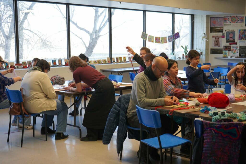 People seated at tables in an art studio using string to create woven art.