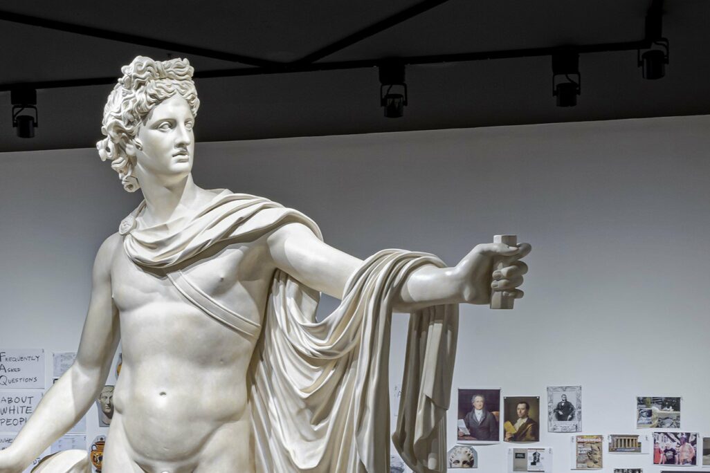 A Marble statue stands in front of a collage of images on the wall that make up a timeline.